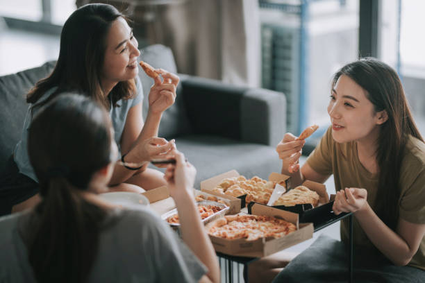 3 asian chinese female friends having pizza for lunch in their living room bonding time - junk food stock pictures, royalty-free photos & images