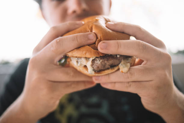 a boy eating a delicious burger in a restaurant - junk food stock pictures, royalty-free photos & images