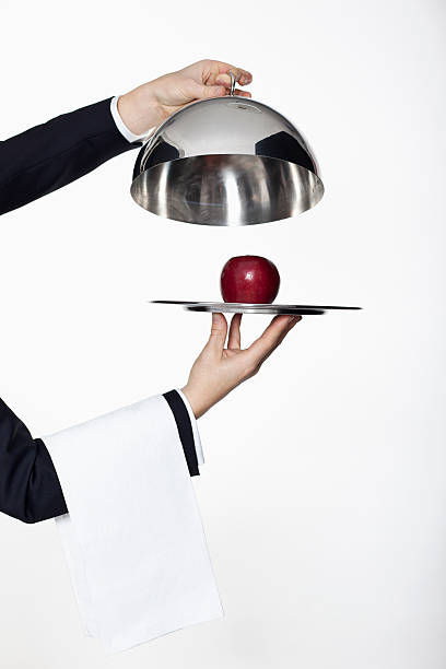 a butler taking the lid off a domed tray, revealing a red apple, focus on hands - food stock pictures, royalty-free photos & images