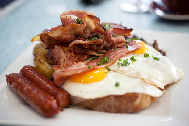 a closeup of eggs, bacon, ham, and sausage on top of toast - junk food stock pictures, royalty-free photos & images
