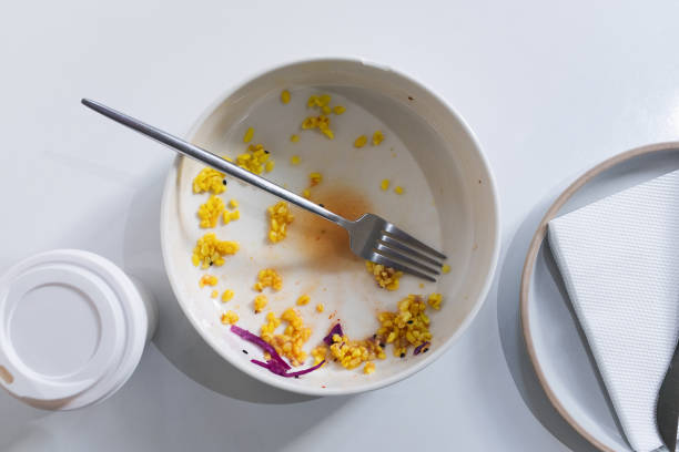 a dirty empty plate and fork on a wooden kitchen or dining table. cutlery is used, symbolizing the end of lunch or dinner. a portion of food eaten, overeating. next to it is a disposable paper coffee mug. completion of lunch 