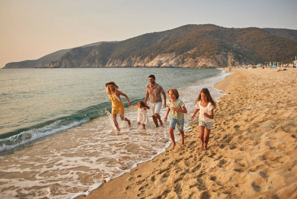 a family run hand in hand down a tropical paradise beach during sunset - travel stock pictures, royalty-free photos & images