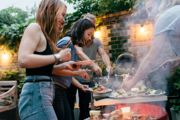 a group of friends helping themselves to food at a summer barbecue - food stockfoto's en -beelden