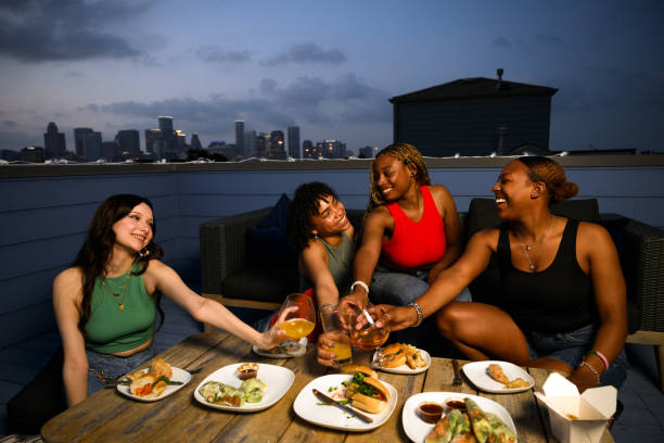 a group of girlfriends perform celebratory toast to friendship and togetherness over take out food on a blue rooftop with skyscrapers at dusk in background - junk food stock pictures, royalty-free photos & images