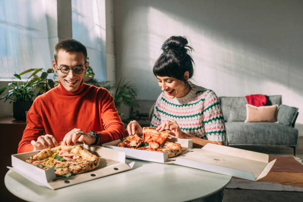 a handsome man and his girlfriend smiling while taking a slice of pizza - junk food stock pictures, royalty-free photos & images