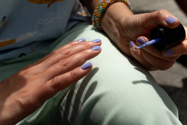 a high school student does a manicure. a woman paints her nails with nail polish in a bright color. an independent manicure in the open air, and not from a cosmetologist. do it yourself. body care during your stay at home, du