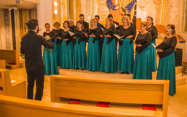 a large group of people dressed in the same formal clothes rehearse before a choral performance with a conductor - concert stock pictures, royalty-free photos & images