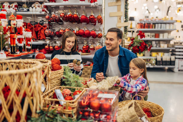 a little girl chooses christmas decorations with her parents. they look at the selection of decorations that are on display in the department store - home decoration stock pictures, royalty-free photos & images