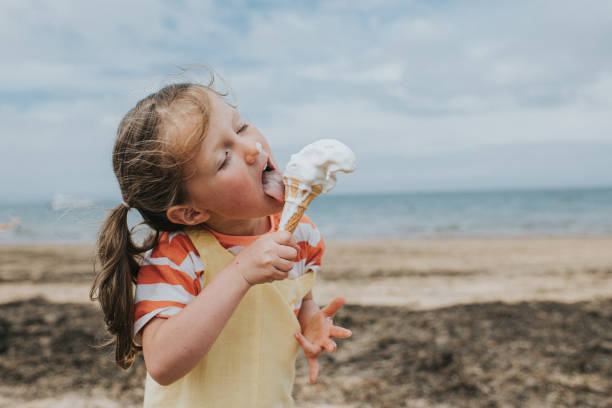 a little girl stands on a beach and eats a melting ice-cream - food fotografías e imágenes de stock