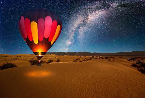 a majestic hot air balloon soars under the stars of the milky way, over the desert - mesquite dunes of death valley national park. moonlight provides luminosity showing the patterns and shapes of the desert landscape. - trave