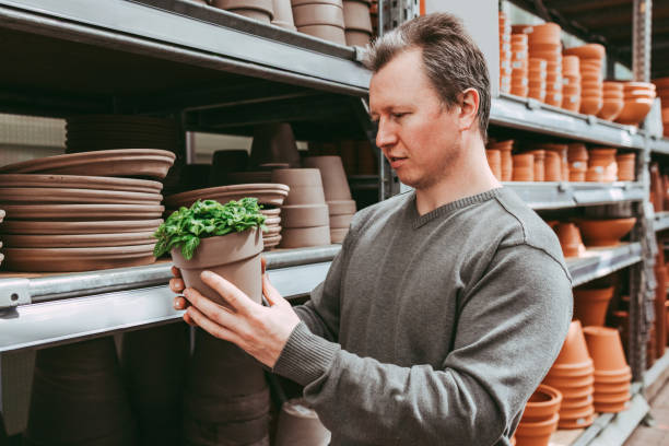 a male gardener chooses a pallet for a home flower in a flower shop or mall. gardening at home as a hobby for men. home gardening - garden decoration stock pictures, royalty-free photos & images