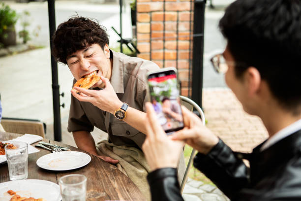 a man has a friend take a picture of him eating pizza on vacation with his smartphone. - food stock pictures, royalty-free photos & images