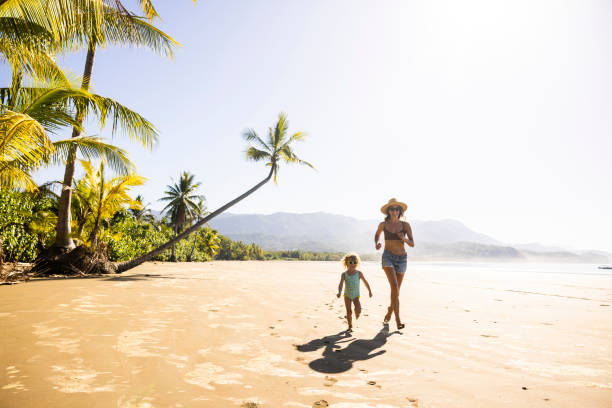 a mother and her daughter running down a palm tree scattered beach in costa rica. - travel stockfoto's en -beelden