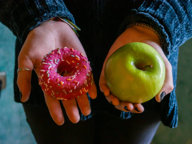 a person with an apple and a donut in their hands - junk food stock pictures, royalty-free photos & images