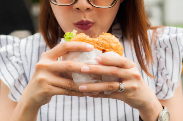 a southeast asian woman is eating hamburger outdoors - junk food stock pictures, royalty-free photos & images
