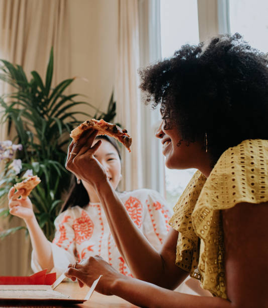 a woman enjoys a slice of pizza with a friend - junk food stock pictures, royalty-free photos & images