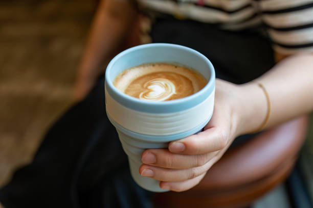 a woman holding a cup of coffee in a reusable mug. - junk food stock pictures, royalty-free photos & images