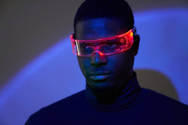 a young african-american man in futuristic fashion glasses with neon light looks away. the concept of the future, computer games, augmented reality, virtual reality, modern technologies, technological progress. - fashion stoc