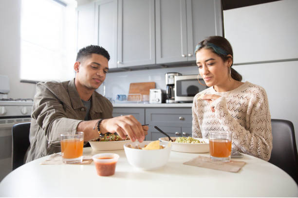 a young latinx brother and sister enjoy eating a mexican salad bowl at the kitchen table, wearing casual clothing. - junk food stock pictures, royalty-free photos & images