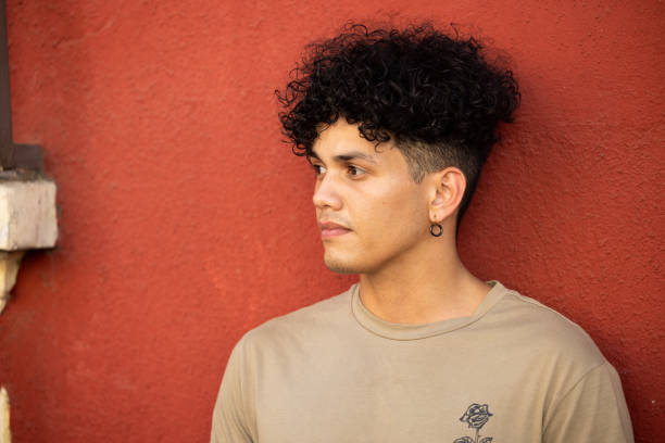 a young man leans against a wall and looks to his right side - hairstyle stock pictures, royalty-free photos & images