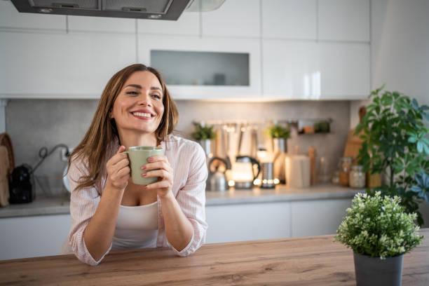 a young woman enjoys her kitchen, dressed in pajamas, drinking her morning coffee - coffee stockfoto's en -beelden