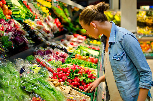 a young woman looking at fresh vegetables in the supermarket - food stock pictures, royalty-free photos & images