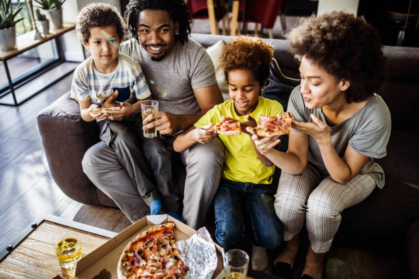 above view of happy black family eating pizza at home. - junk food stock pictures, royalty-free photos & images