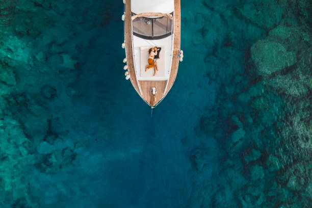 aerial drone view of couple in love on board of luxury yacht anchored in tropical paradise bay with emerald clear water - travel stock pictures, royalty-free photos & images