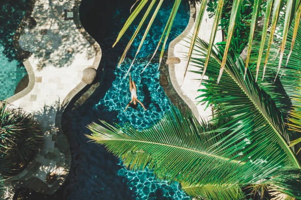 aerial drone view of woman floating on water surface in luxury pool in tropical garden - travel stock-fotos und bilder