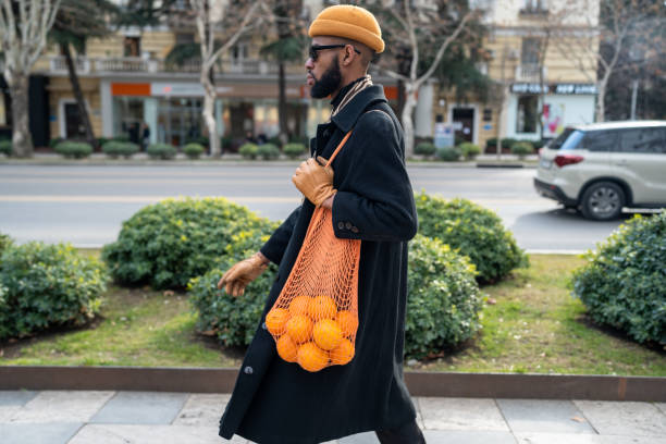 african american walking city street carrying oranges in reusable cotton mesh shopping bag - food stock pictures, royalty-free photos & images