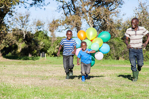 african boy with balloons being chased by father and brother - garden decoration stock pictures, royalty-free photos & images