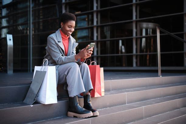 african woman using the mobile sitting with shopping bags - fashion stock pictures, royalty-free photos & images