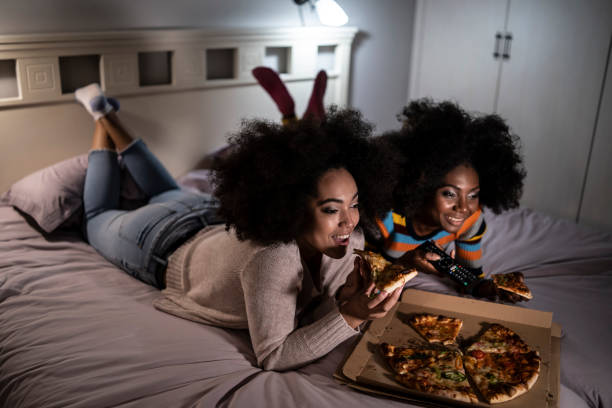 african women lying on bed and eating pizza - junk food stock pictures, royalty-free photos & images