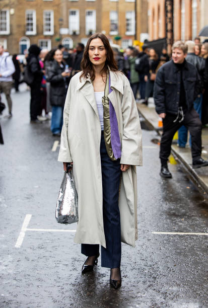 Alexa Chung wears trench coat, silver sequined bag, blue striped pants outside JW Anderson during London Fashion Week February 2024 on February 18,...