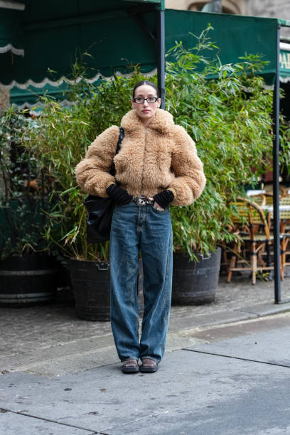 Alexandra Guerain wears black glasses, silver hoop earrings, light brown faux fur zipped cropped jacket, black long sleeve shirt, shiny black leather...