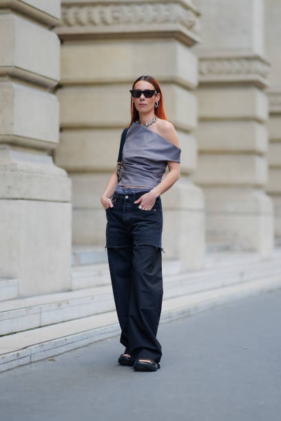 Alice Barbier wears black sunglasses, silver earrings, silver chunky necklace, a gray half shoulder top, black and gray pattern/print Louis Vuitton...