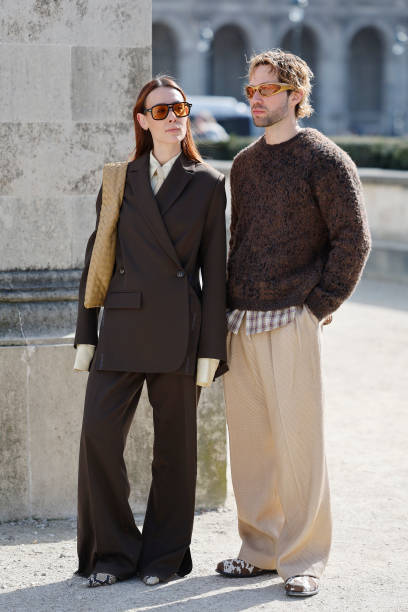 Alice Barbier wears brown suit, beige shirt and tie, beige Bottega Veneta bag, snake skin print heels, and js Roques wears brown sweater, beige...