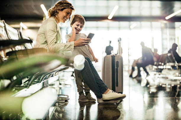 alleinerziehende mutter und sohn benutzen handy, während sie auf ihren transport im abflugbereich warten. - travel stock-fotos und bilder