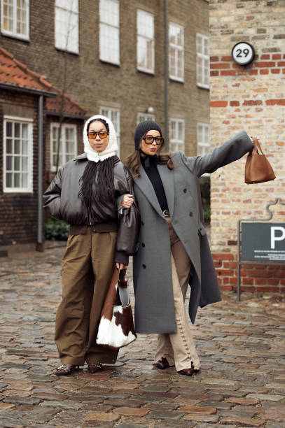 Amaka Hamelijnck wears wide brown pants, dark brown leather jacket, white hat and cow print bag and Benthe Liem wears beige pants, black turtle neck,...