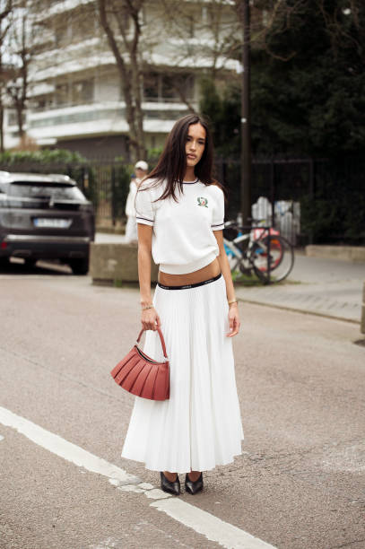 Amalie Bladt wears white maxi pleated skirt, white short sleeve top and red bag outside the Lacoste fashion show during the Womenswear Fall/Winter...