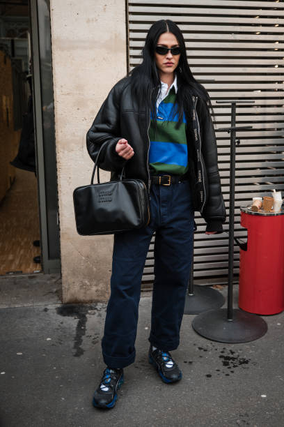 Amelia Gray Hamlin wears blue and green polo neck top, black leather jacket, blue pants, Miu Miu black. Bag, black and blue sneakers, outside...