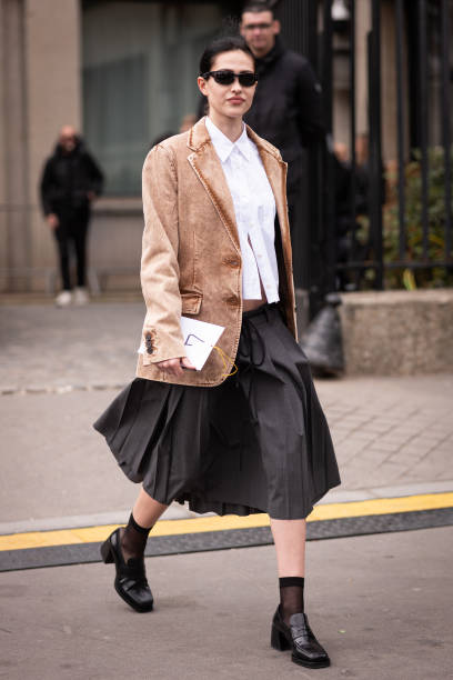 Amelia Gray wears a beige denim Miu Miu blazer, white shirt, black skirt, black loafers and blue Miu Miu bag, outside Miu Miu, during Paris Fashion...