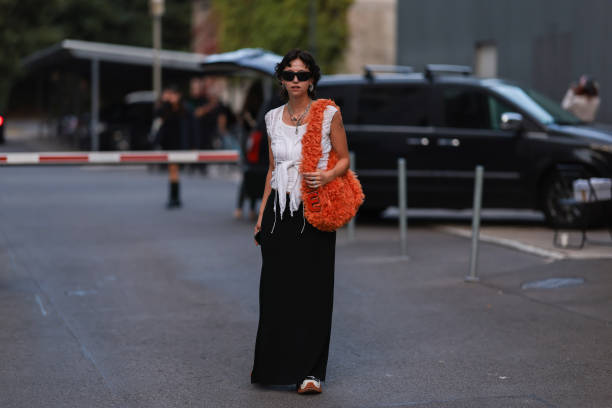 Amelie Kahl is seen wearing black shades, silver earrings and necklaces, white top, fluffy orange Miu Miu shoulder bag, black long skirt and black...