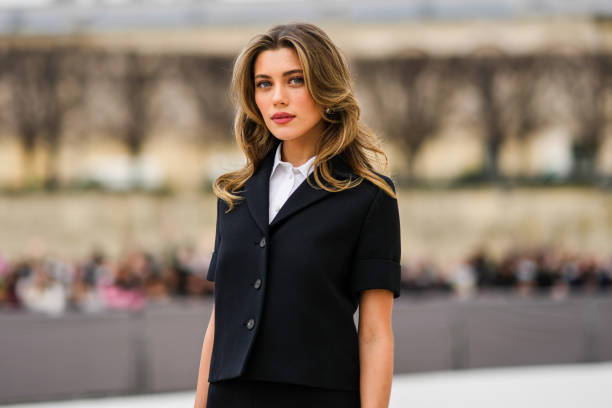 Amelie Zilber wears a white short sleeves shirt from Dior, a black short sleeves buttoned jacket from from Dior, a black short skirt from from Dior,...