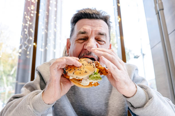 an adult man eating a burger in a cafe. - junk food stock pictures, royalty-free photos & images