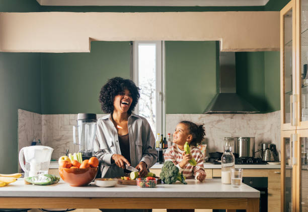 an african-american single mother preparing vegan lunch in the kitchen and smiling with her little daughter - food stock pictures, royalty-free photos & images