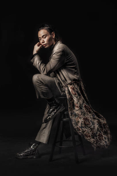an asian chinese male sitting on a stool with fashion clothe looking cool at the camera with black background studio shoot - fashion stock pictures, royalty-free photos & images