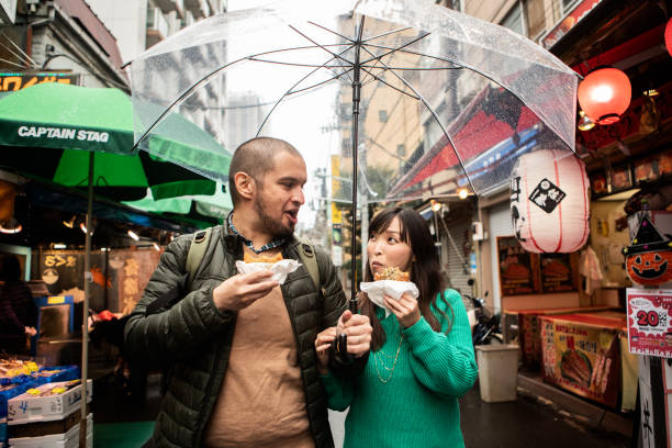 an internationally married couple who came to tsukiji for sightseeing while eating fried food - travel stock pictures, royalty-free photos & images