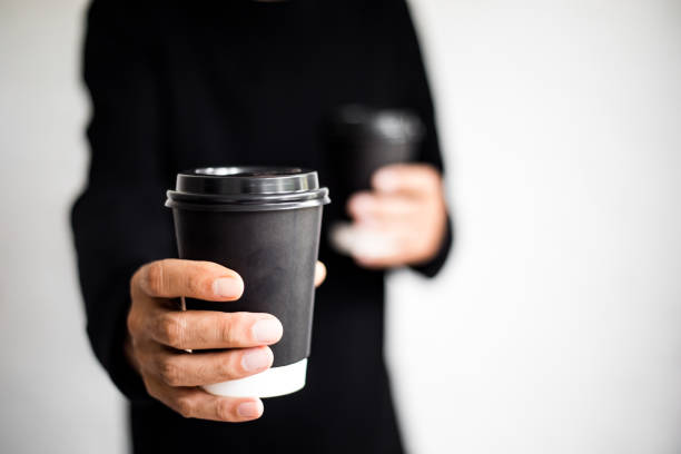 an unrecognizable man holding two disposable and black paper coffee cups - junk food stock pictures, royalty-free photos & images