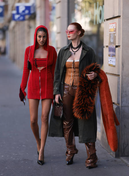 Anaa Saber is seen wearing black high heels, a red bra and a long red jacket with a hood next to Jordan Grant wearing brown heels, a red fur, a green...